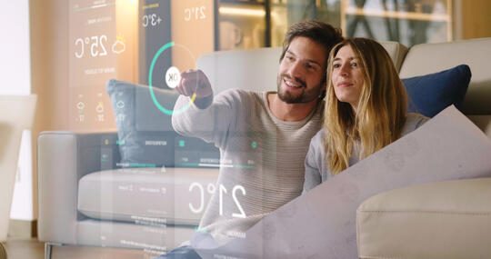 Par i sofa ser på skjerm med data for huset